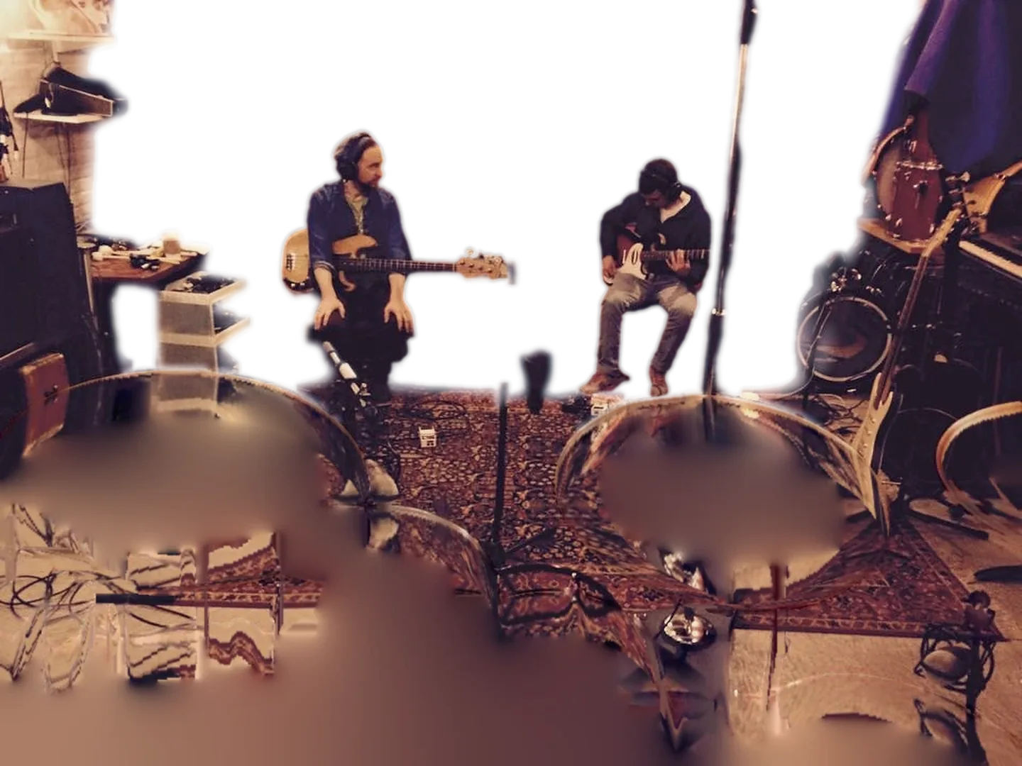 A live tracking room seen from behind the drum kit: Alex on bass and a guitarist, both in headphones.